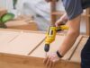 Custom furniture assembling handyman fixing fasteners on wooden cabinet back side with professional screwdriver quality carpentry services specialist working with wood materials